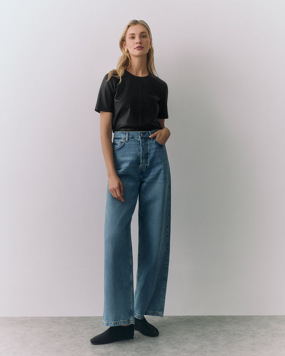 Person wearing t-shirt, wide-leg jeans, and shoes standing against plain background