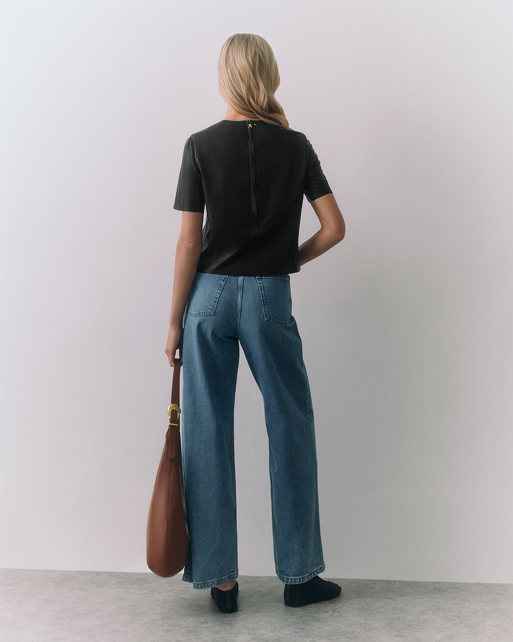 Person in jeans and tee holding a travel bag, facing away from the camera