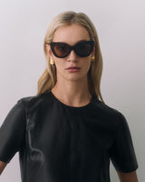 Woman wearing sunglasses and earrings, dressed in a leather top