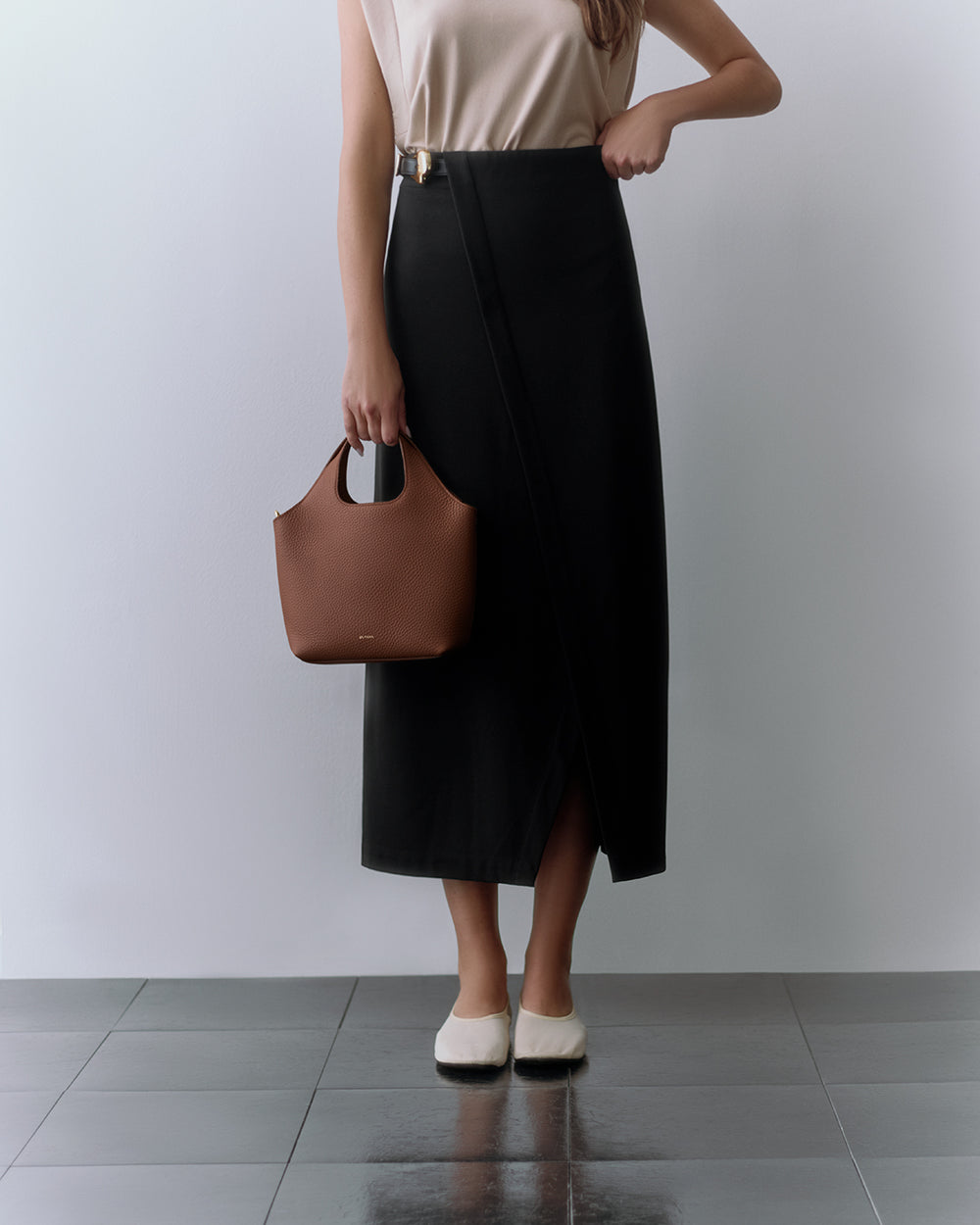 Person in long skirt holding a small handbag, standing on a tiled floor.