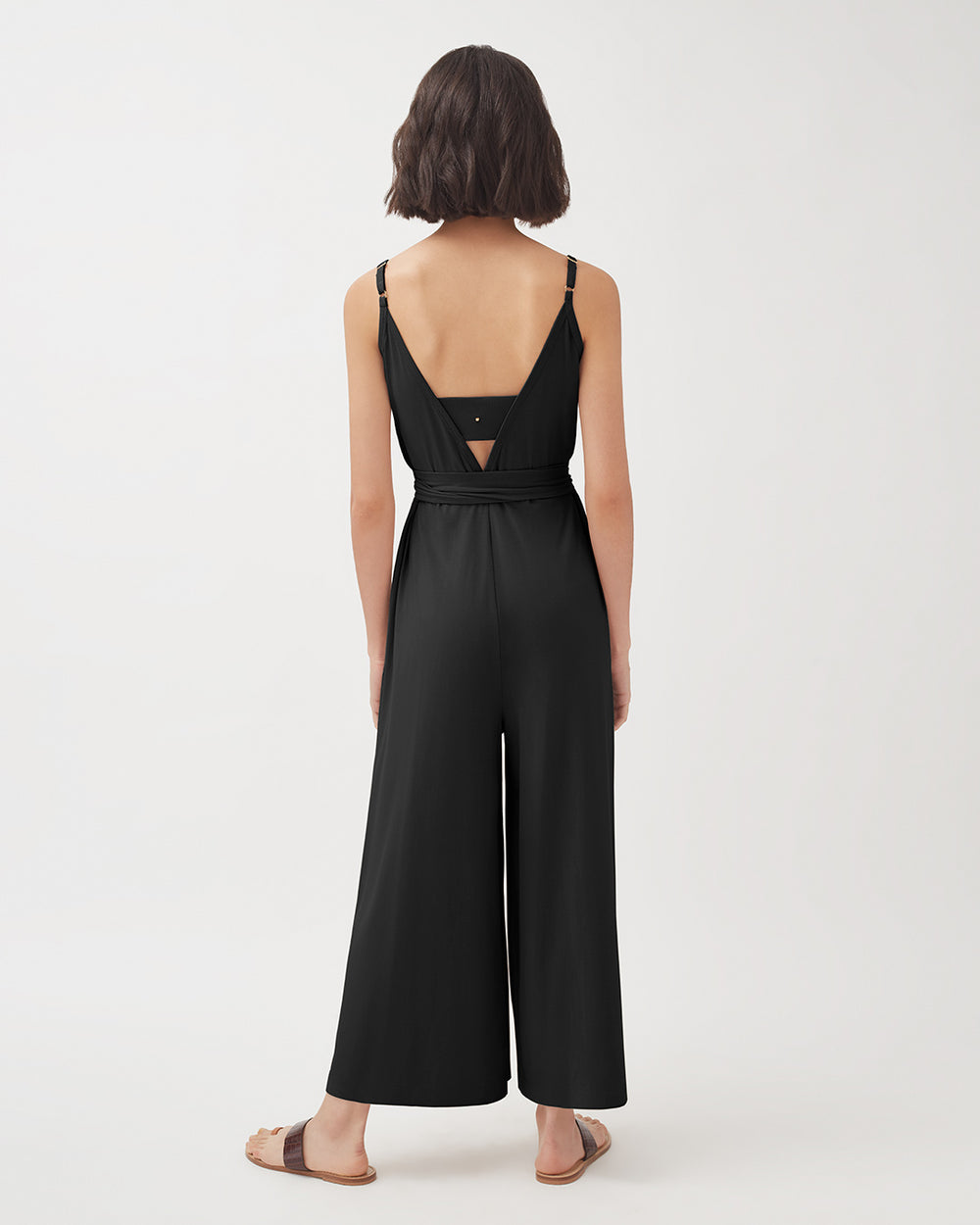 Woman in a jumpsuit standing with her back facing the camera.
