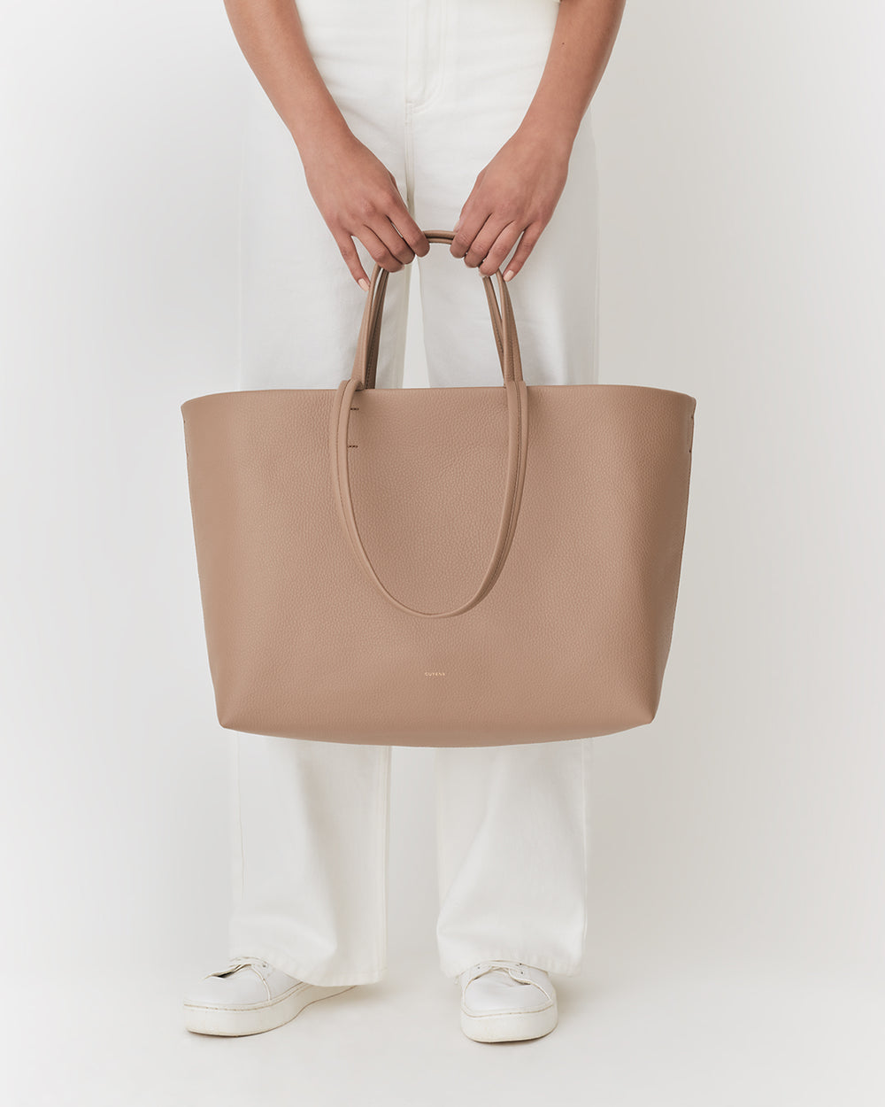 Person holding a large tote bag, standing in white pants and shoes.