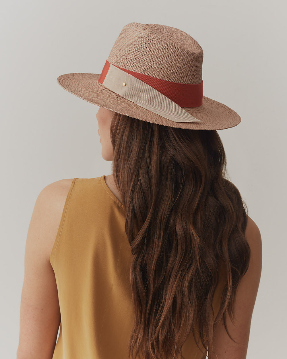 Woman with wavy hair wearing a hat, viewed from behind.
