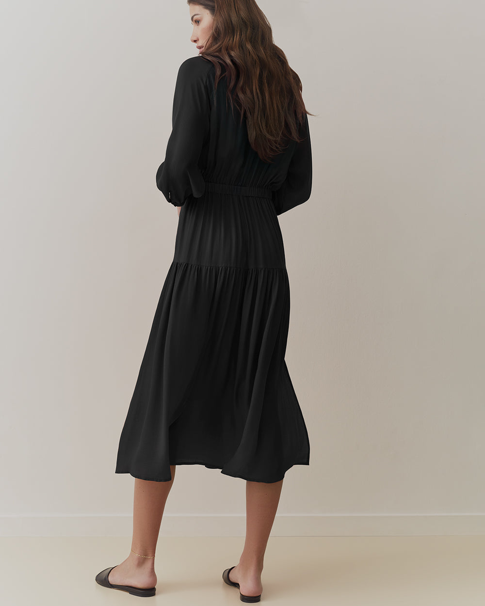 Woman in long-sleeved dress standing, viewed from behind.
