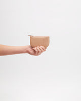 Hand holding a small zippered pouch against plain background.