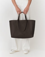 Person holding large tote bag by handles, wearing pants and shoes.