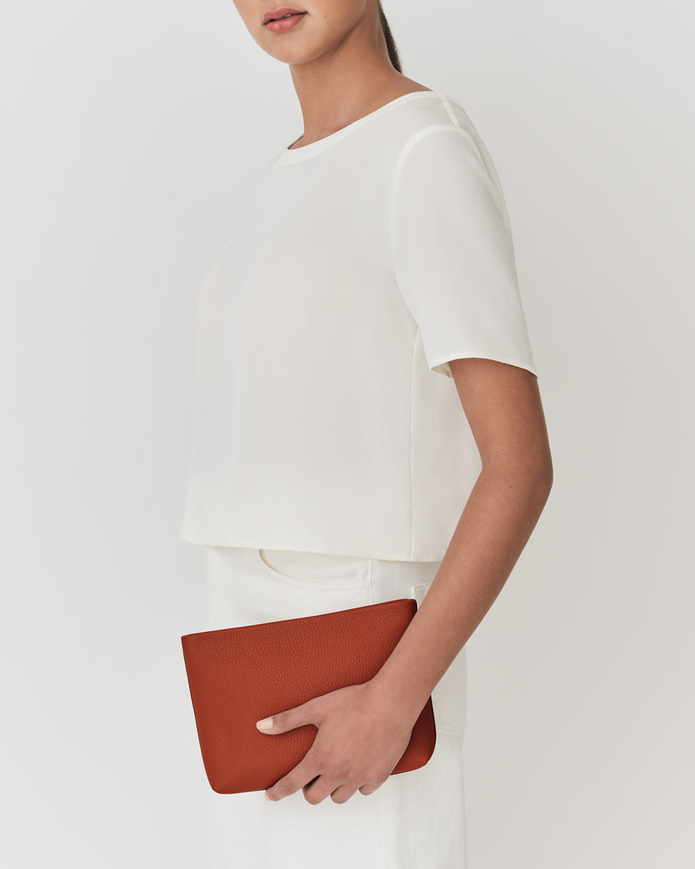 Person holding a pouch, wearing a short-sleeved shirt and a skirt.