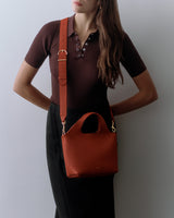 Person posing with a crossbody bag, hands on hips, wearing a short-sleeve shirt and skirt.