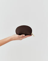 Hand holding a small leather pouch with a zipper.