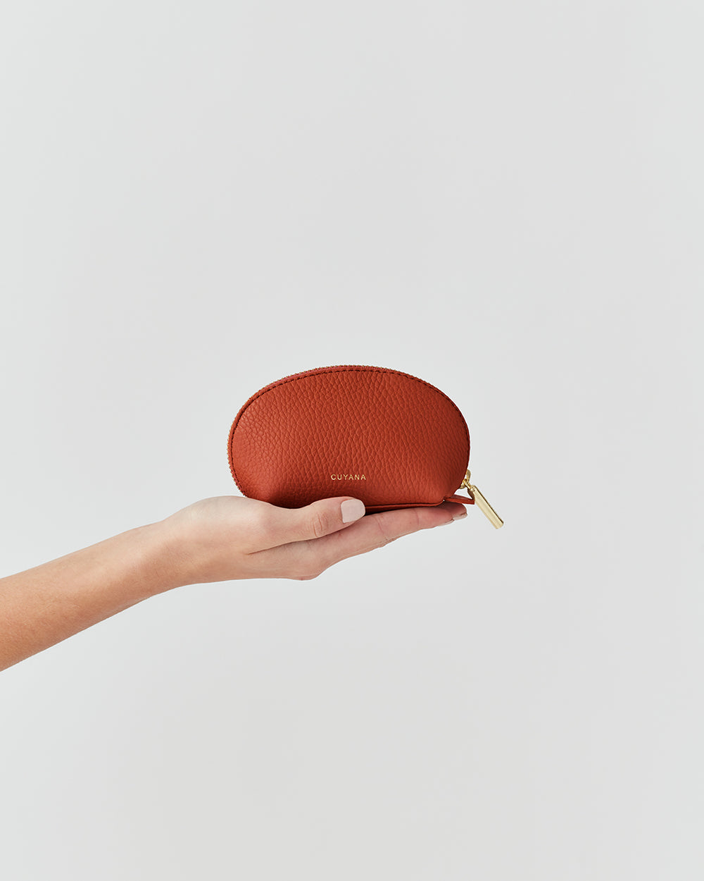 Hand holding a small leather pouch with a zipper.