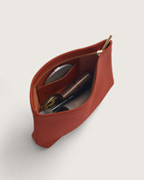 Open leather pouch with cosmetics inside, displaying a zipper and compact mirror.