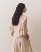 Person wearing loose top and wide-leg pants standing against plain backdrop