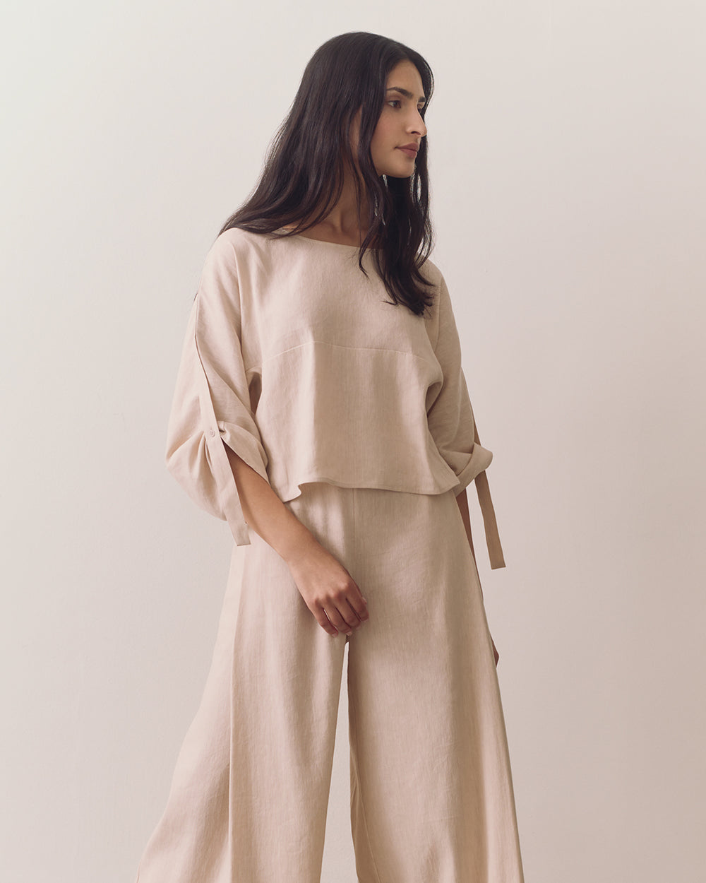 Person wearing loose top and wide-leg pants standing against plain backdrop
