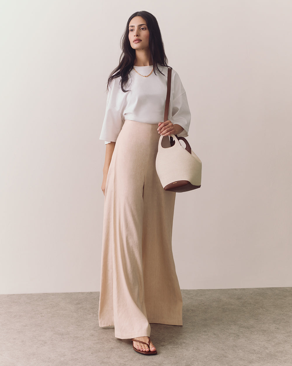 A person in a shirt and wide-leg trousers holding a bag on their shoulder.