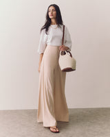 A person in a shirt and wide-leg trousers holding a bag on their shoulder.