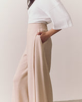 Person wearing a loose top and wide-leg trousers standing with hand in pocket.