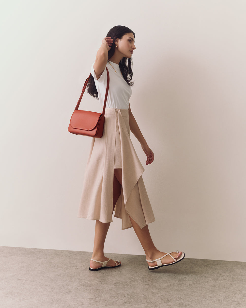 Woman walking with shoulder bag wearing a sleeveless top and flowing skirt with slit.