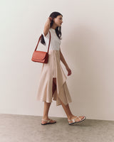 Woman walking with shoulder bag wearing a sleeveless top and flowing skirt with slit.