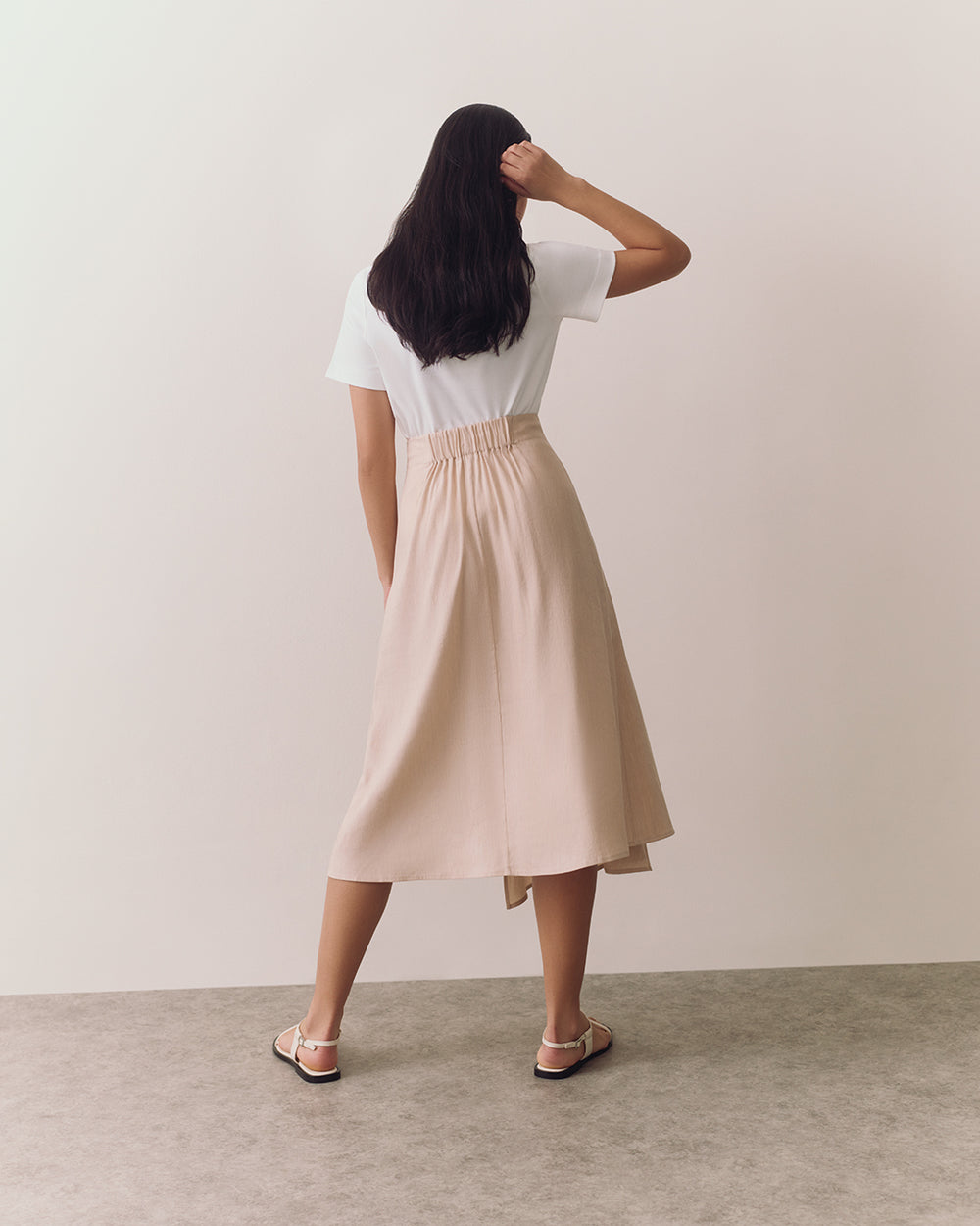 Person wearing a T-shirt and skirt, facing away, standing on a plain floor.