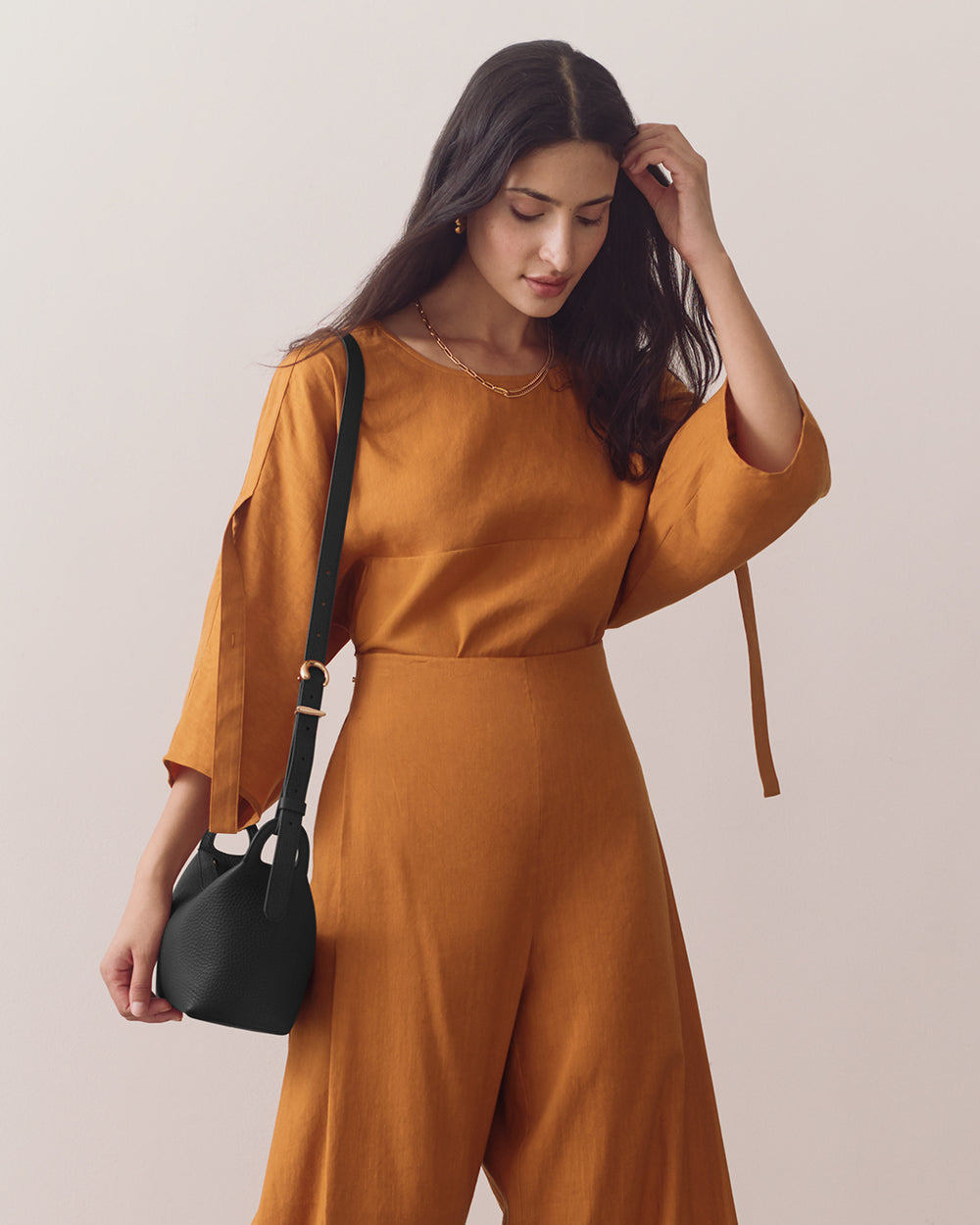 Person in a matching outfit holds a shoulder bag.