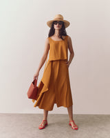 Person in a sleeveless top and flowy skirt holding a small handbag, standing indoors