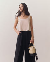 Person in sleeveless top and wide pants holding a woven bag.