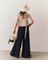 Person wearing a sleeveless top and wide-leg pants, holding a small handbag, wearing a wide-brim hat