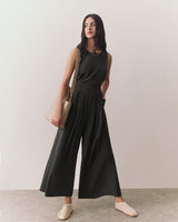 Person in sleeveless outfit with wide pants, holding a shoulder bag, standing indoors.