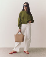 Person wearing sunglasses, holding a bag, in a relaxed jacket and sandals.