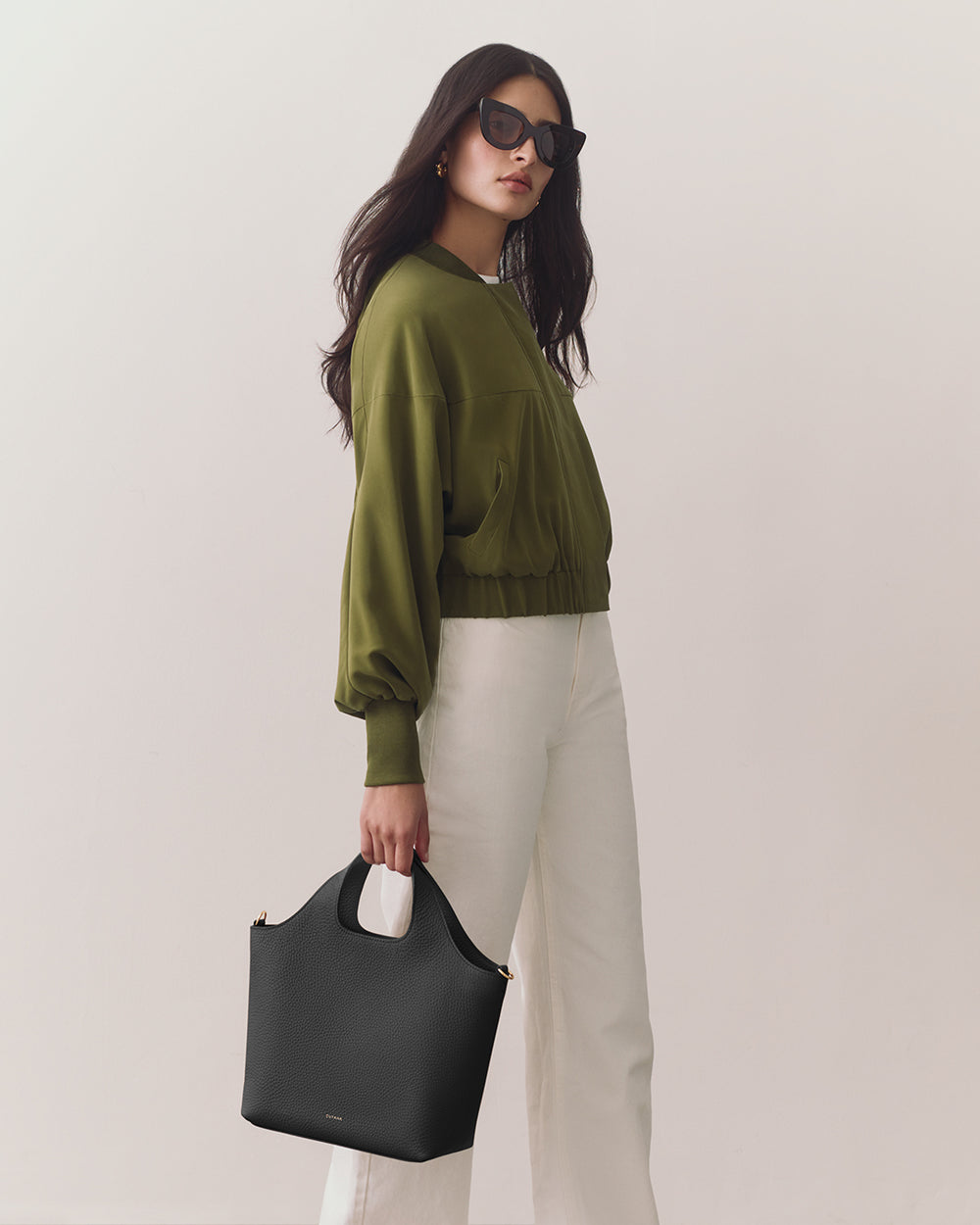 Person wearing jacket and pants holding a handbag, wearing sunglasses