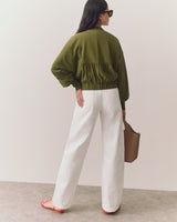Person in long pants and a relaxed jacket holding a handbag, facing away.