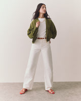 Person wearing open jacket, t-shirt, wide pants, sandals, and necklace standing confidently