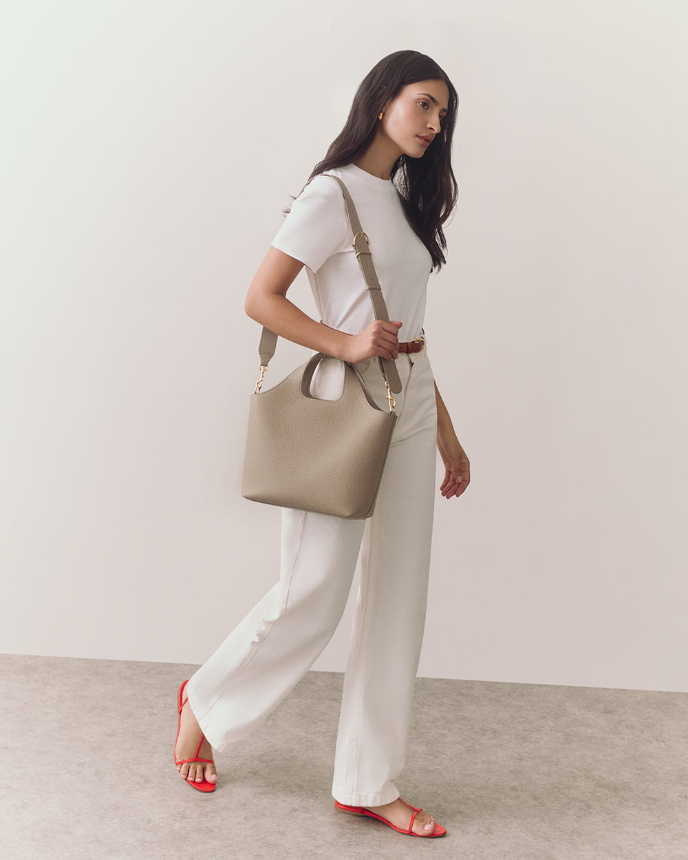 Person walking with a shoulder bag wearing a T-shirt and pants.