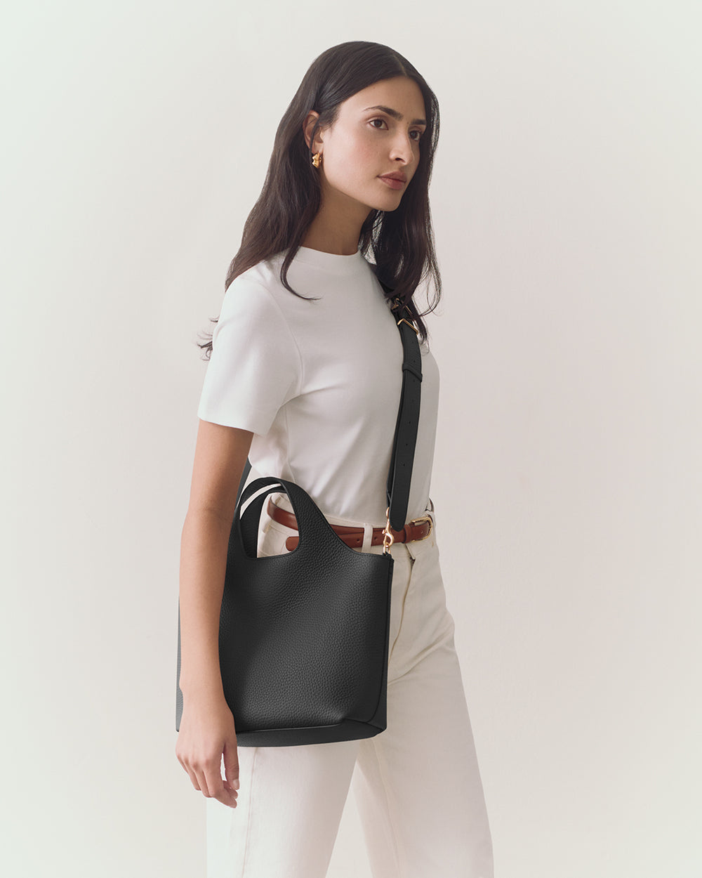 Person holding a handbag stands against a plain background.