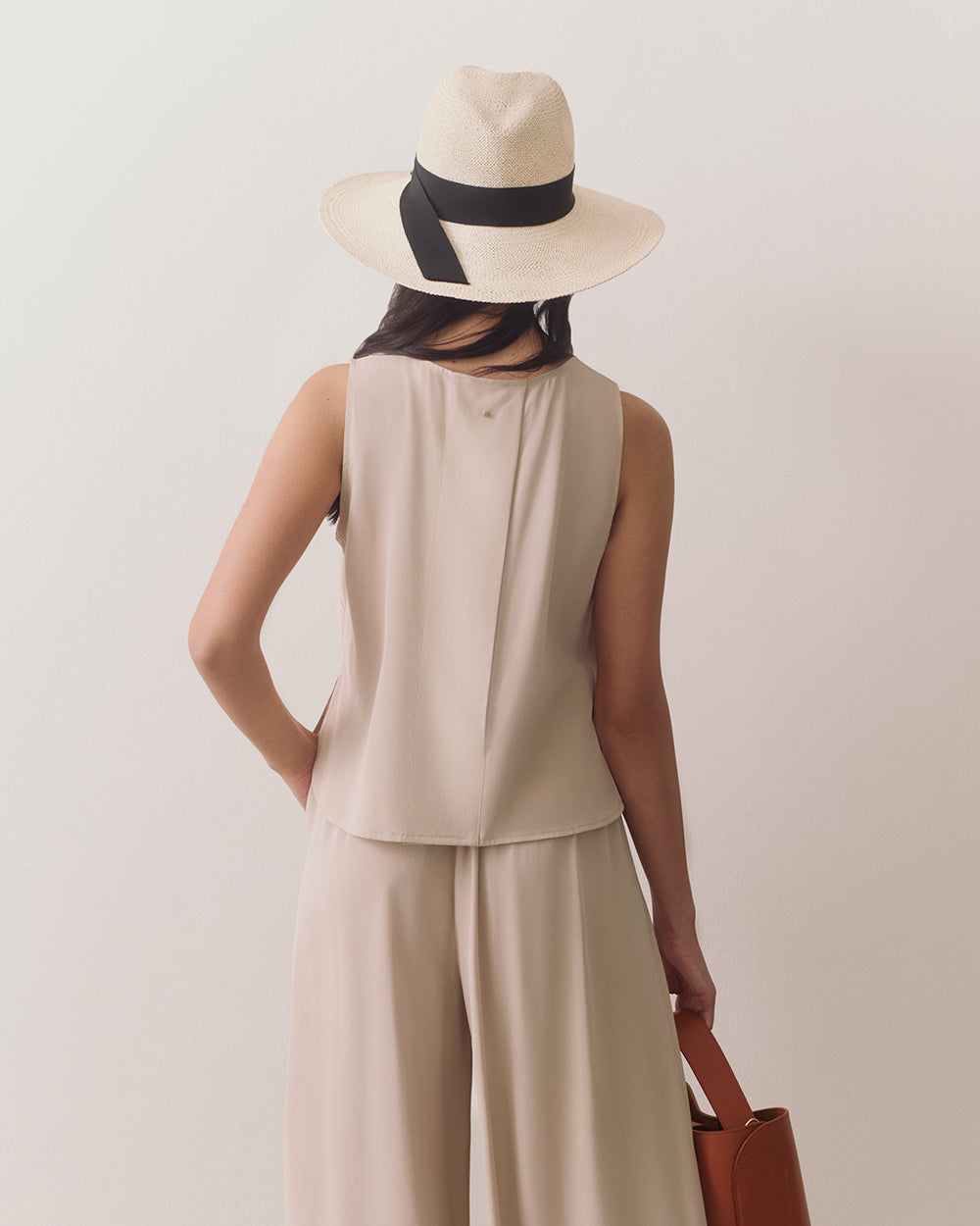 Person wearing a hat and sleeveless top with loose pants, holding a rectangular bag.