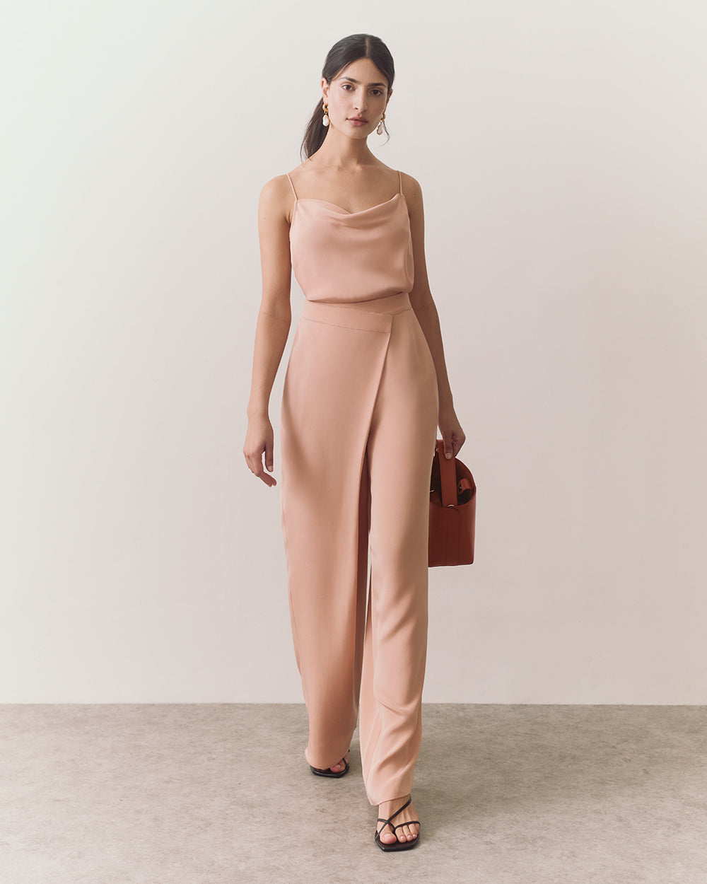 Woman walking in sleeveless top and wide-leg pants holding a bag.