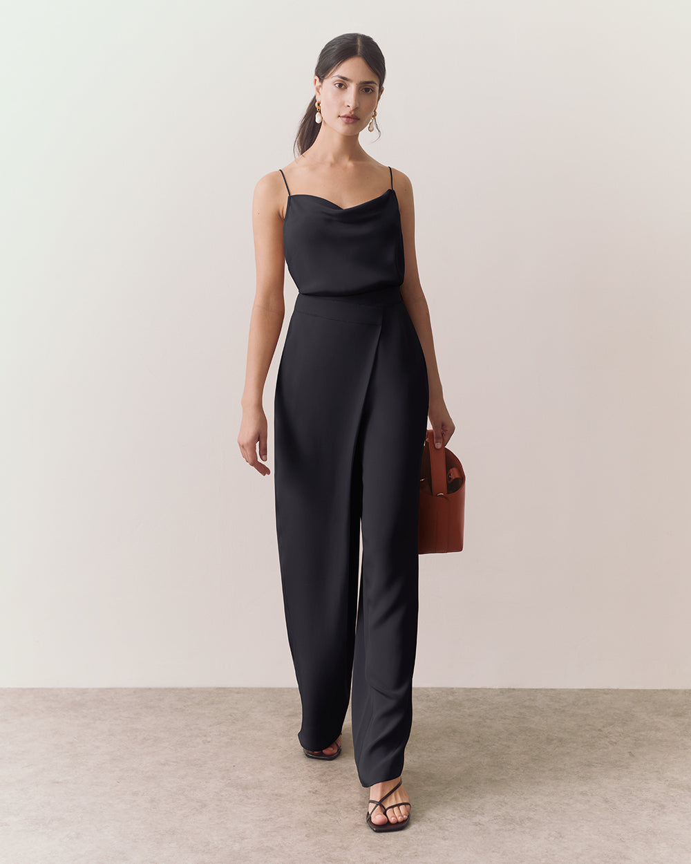 Person wearing a cami, wide leg pants, and a handbag, walking indoors.
