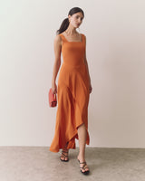 Person in long dress holding a clutch, walking on a plain background.