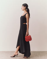 Person in a long dress holding a small handbag, standing sideways.
