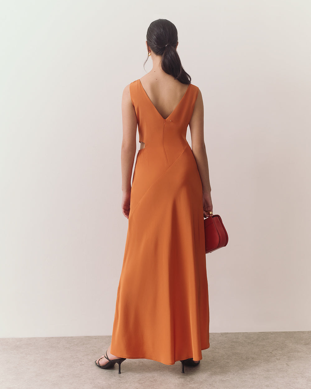 Person in long dress holding a handbag, standing on a textured floor facing away.