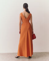 Person in long dress holding a handbag, standing on a textured floor facing away.