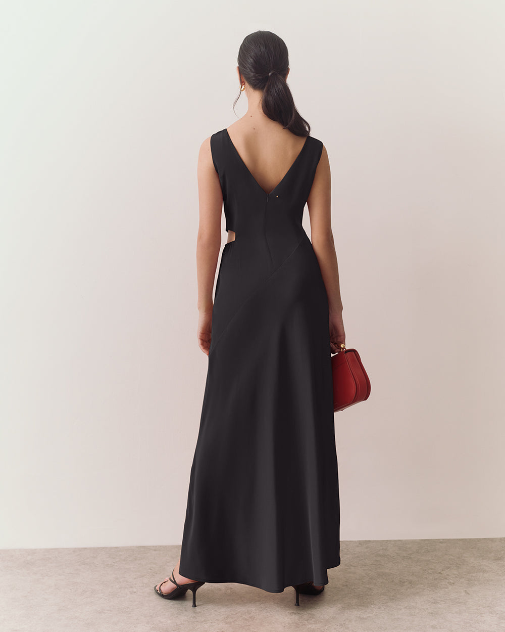 Person in long dress holding tote bag, standing on a plain floor.