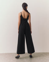 Person in sleeveless jumpsuit facing away, standing on a plain floor.