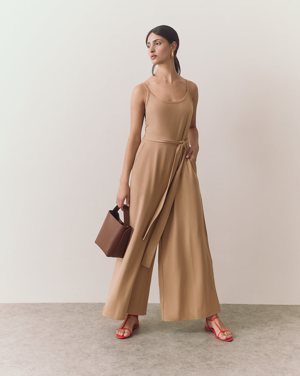 Person in jumpsuit holding a handbag, wearing sandals.