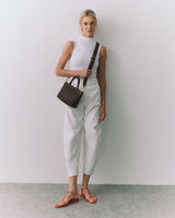 Person wearing a sleeveless top, pants, sandals, and shoulder bag.