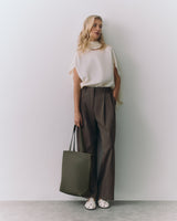 Person standing, wearing a sleeveless top and wide pants, holding a tote bag.