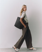 Person standing with a large tote bag over shoulder wearing wide-leg pants and sandals