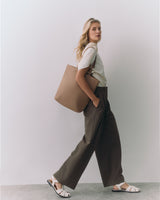 Person standing with large bag over shoulder wearing wide-leg pants and sandals.