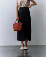 Person carrying a handbag, wearing a sleeveless top and long skirt, standing on tiled floor.