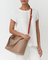 Person wearing a plain outfit holding a handbag with a long strap.